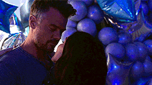 a man and a woman are standing next to each other in front of a bunch of blue balloons .