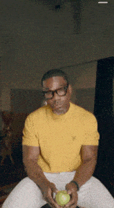 a man wearing glasses and a yellow shirt holds an apple
