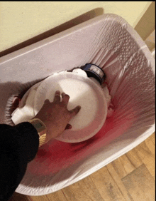 a person is reaching into a trash can with a paper plate