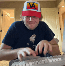 a man wearing a hat with the letter a on it is typing on a keyboard