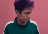 a man with purple hair is standing in front of a pink background