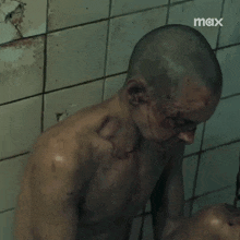 a man with a shaved head is standing in front of a tiled wall with the word max written on it .
