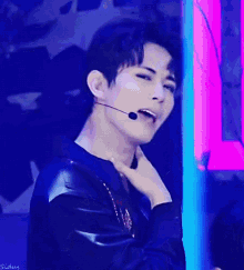 a young man wearing a black jacket and a microphone is making a face .