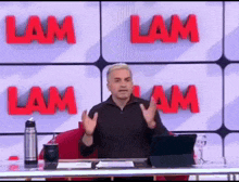 a man is sitting at a desk in front of a wall that says lam .
