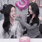 a girl is feeding another girl a piece of cake in front of balloons that say 3