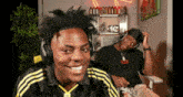 a man wearing headphones is smiling while another man sits behind him