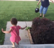 a little girl in a pink dress is walking down a sidewalk next to a woman holding a purse