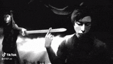 a black and white photo of a man holding a sword in front of a woman .