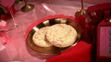 two cookies with pink sprinkles on them on a gold plate