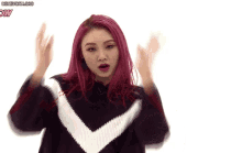 a woman with pink hair is wearing a black and white sweater and making a funny face .