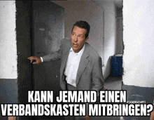 a man in a suit is standing in front of a door with the words kann jemand einen verbandskasten mitbringen