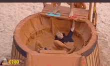 a man is laying in a muddy pool with a sign that says 02:03 on it .