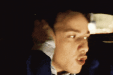 a man in a suit and tie is driving a car and making a funny face