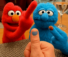 elmo and cookie monster are sitting next to a person 's finger