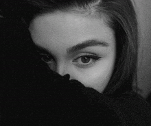 a black and white photo of a woman covering her face with a black sweater