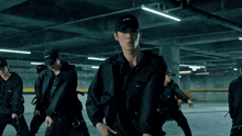a group of men are dancing in a parking garage and one of them is wearing a black hat with the word prada on it