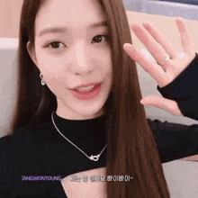 a close up of a woman wearing a necklace and earrings waving her hand .