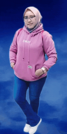 a woman wearing a pink hoodie that says j.m.l.c.s. stands with her hands in her pockets