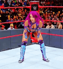 a woman with purple hair is standing in a wrestling ring with a crowd watching .
