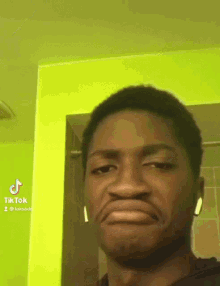 a man wearing ear buds is making a funny face in front of a green wall with tik tok written on the bottom