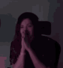 a woman is covering her face with her hands while sitting in a chair in a dark room .