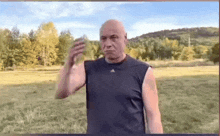 a bald man wearing a black adidas tank top stands in a field