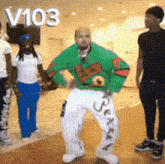 a man in a green sweater and white pants is dancing in front of a group of people with the number 103 above him
