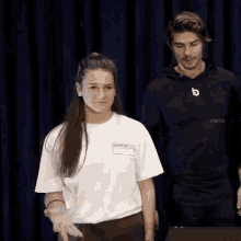 a man and a woman are standing in front of a blue curtain and the man is wearing a nisbar sweatshirt