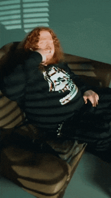 a man with red hair is laying on a couch wearing a shirt that says ' t.t. '