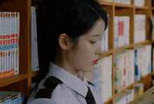 a woman stands in front of a shelf of books including one titled " tokyo ghoul "