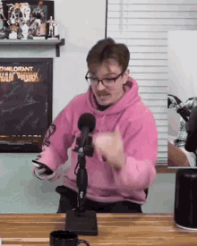 a man wearing a pink hoodie and glasses is sitting in front of a microphone .