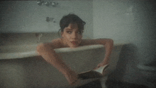 a woman is laying in a bathtub holding a book