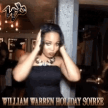a woman in a black dress is standing in front of a sign that says william warren holiday soiree on it