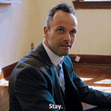 a man in a suit and tie is sitting at a table with the words stay above him