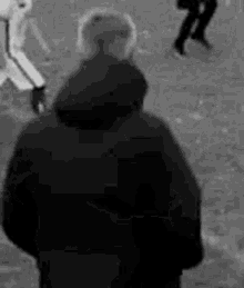 a black and white photo of a man standing on a field watching a baseball game .