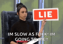 a woman is sitting in a chair holding up a sign that says lie