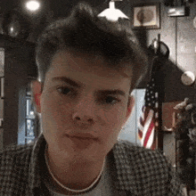 a young man wearing a plaid shirt and pearl necklace looks at the camera