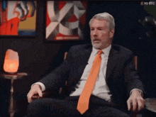 a man in a suit and orange tie is sitting in front of a rd btc sign