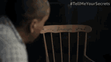 a man is sitting in a wooden chair with a name written on the back of it .