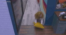 a woman is holding a yellow pillow in a hallway with the number 9 on the desk behind her
