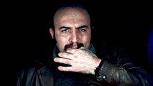 a man with a beard and a leather jacket is covering his mouth with his hand
