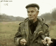 a man is smoking a cigarette in a field while another man holds a cigarette in his hand .