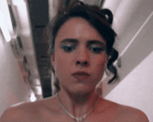 a woman wearing a necklace and earrings looks at the camera