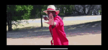 a man wearing a hat and a red robe is making a stop sign with his hand .