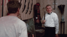 a man in a tuxedo is holding a sword in front of a wall of samurai armor