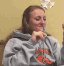 a woman in a gray hoodie is brushing her teeth