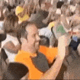 a man in an orange shirt is taking a picture of a crowd of people at a concert .