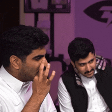 a man covering his mouth with his hand and another man looks on