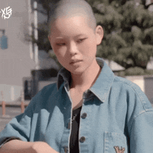 a woman with a shaved head wears a denim jacket