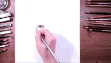 a person is drawing an eye on a piece of paper with pencils on the table